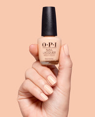 Hand holding OPI Suzi Take a Vow Nail Lacquer in a soft peach nude shade, with matching glossy manicure against a peach background for elegant fall nail colors.