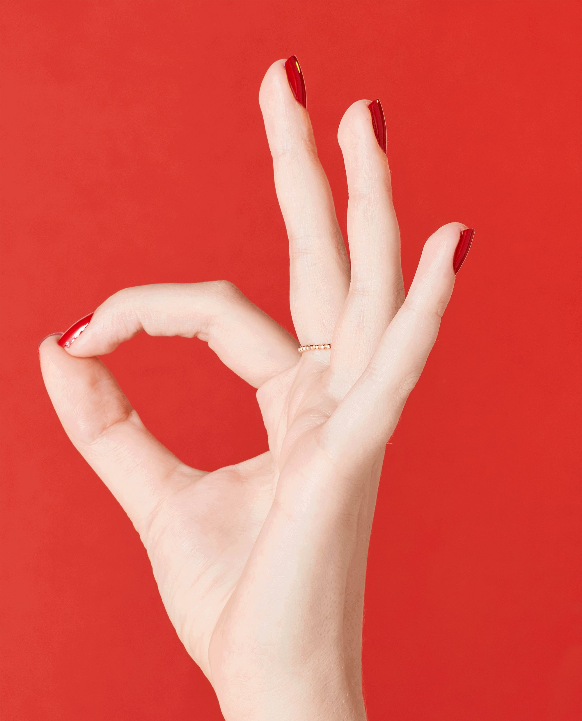 Hand forming an OK sign shows glossy red nails painted with OPI Big Apple Red nail lacquer, against a matching bright red background, highlighting the vibrant nail polish gift set color and smooth salon-quality finish.