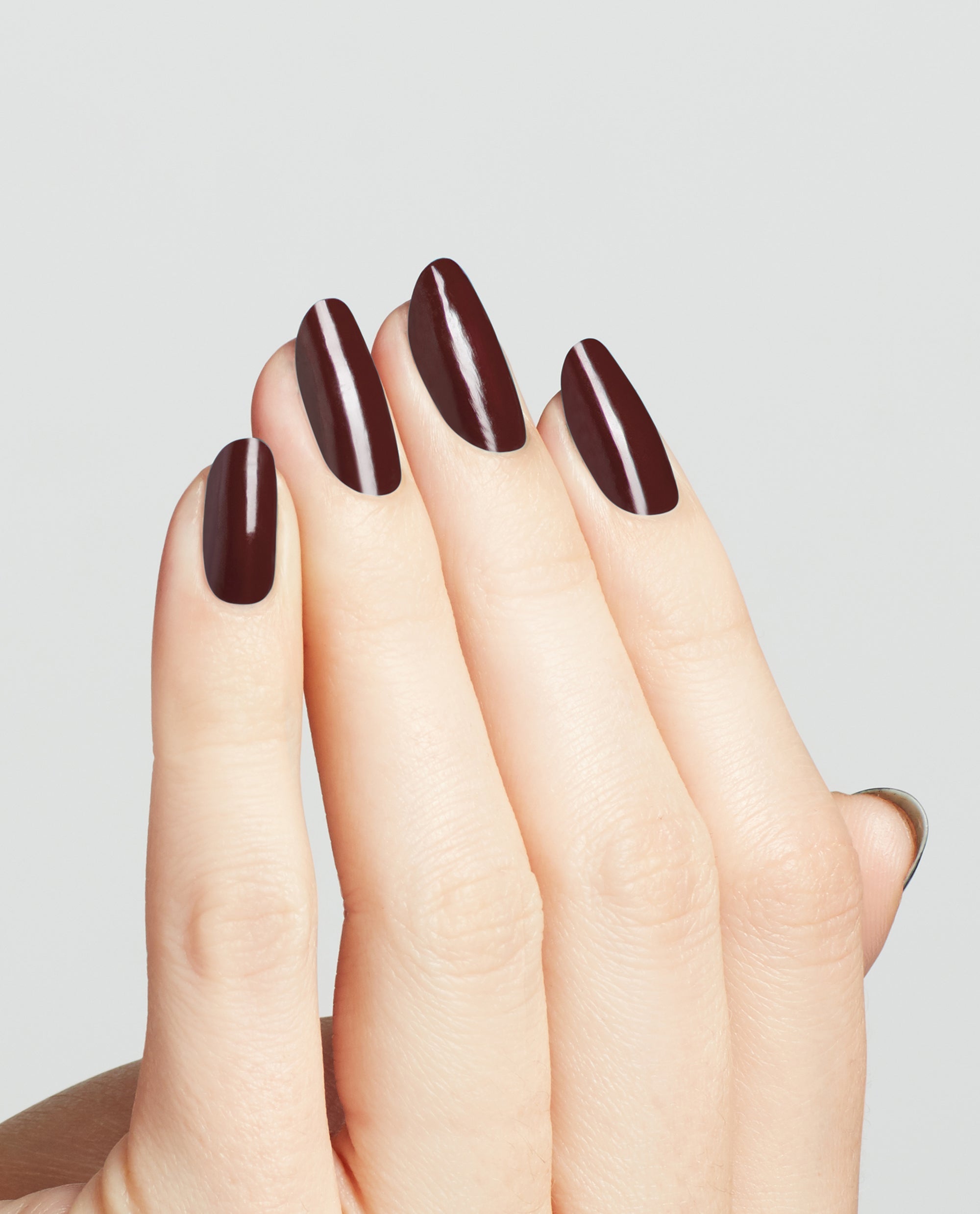Hand shows long oval nails painted in OPI nail polish Complimentary Wine, a deep burgundy nail lacquer with a glossy finish, against a clean light gray background for a modern salon-quality manicure look.