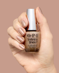 OPI Infinite Shine My Private Yacht polish bottle held by a hand with matching champagne glitter manicure, showcasing a gel-like fall nail color on a warm nude background.