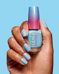 Hand with glossy light blue manicure holds OPI Snap Your Fingers RapiDry nail polish bottle with blue-to-pink ombre cap against a bright blue background, showcasing the nail polish gift set color and sleek product packaging.