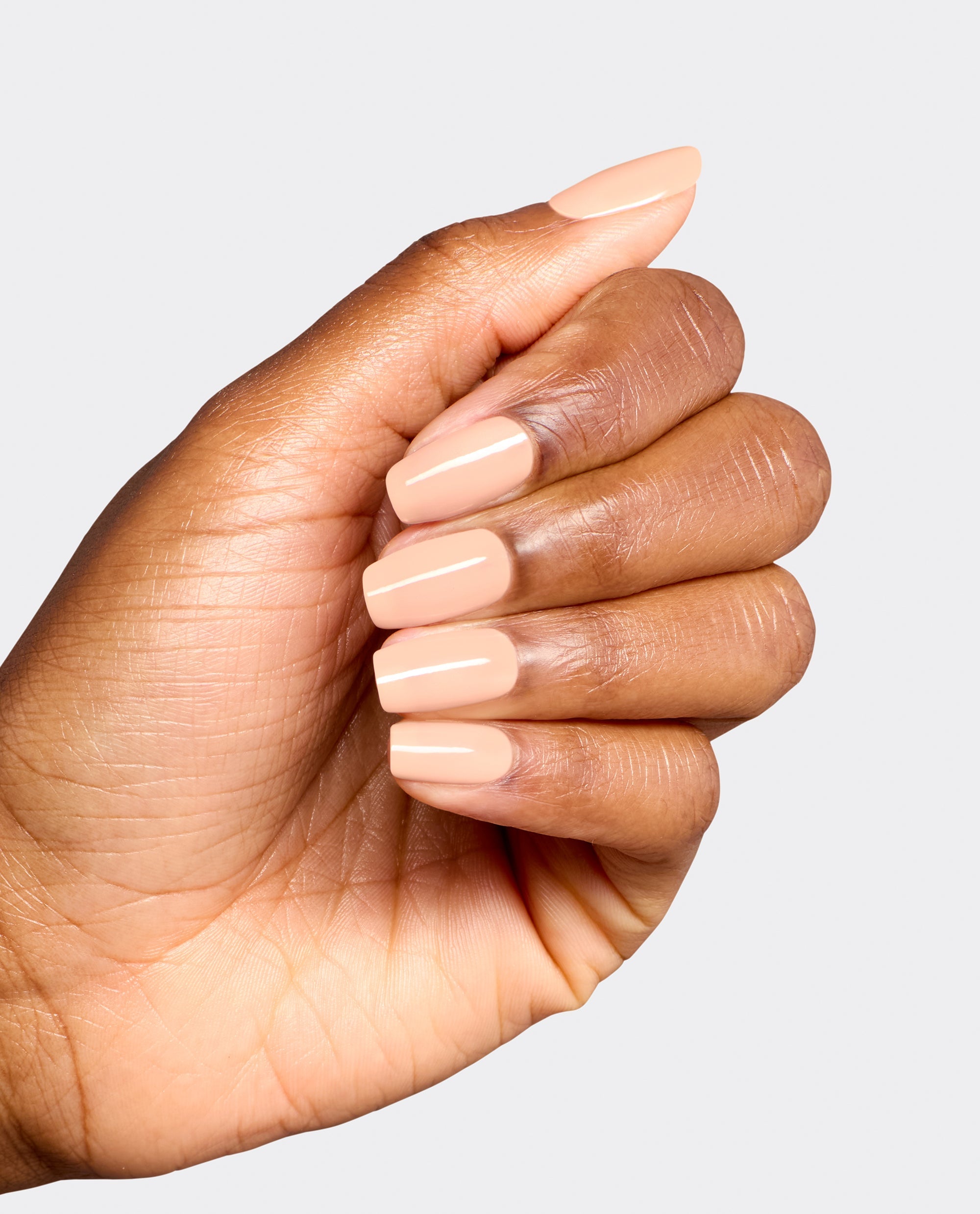 Hand modeling glossy peach-nude OPI Suzi Take a Vow Nail Lacquer on short square nails, showcasing a soft neutral shade for fall nail colors against a light gray background.